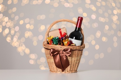 Wicker basket with gifts, wine and food against blurred festive lights. Space for text