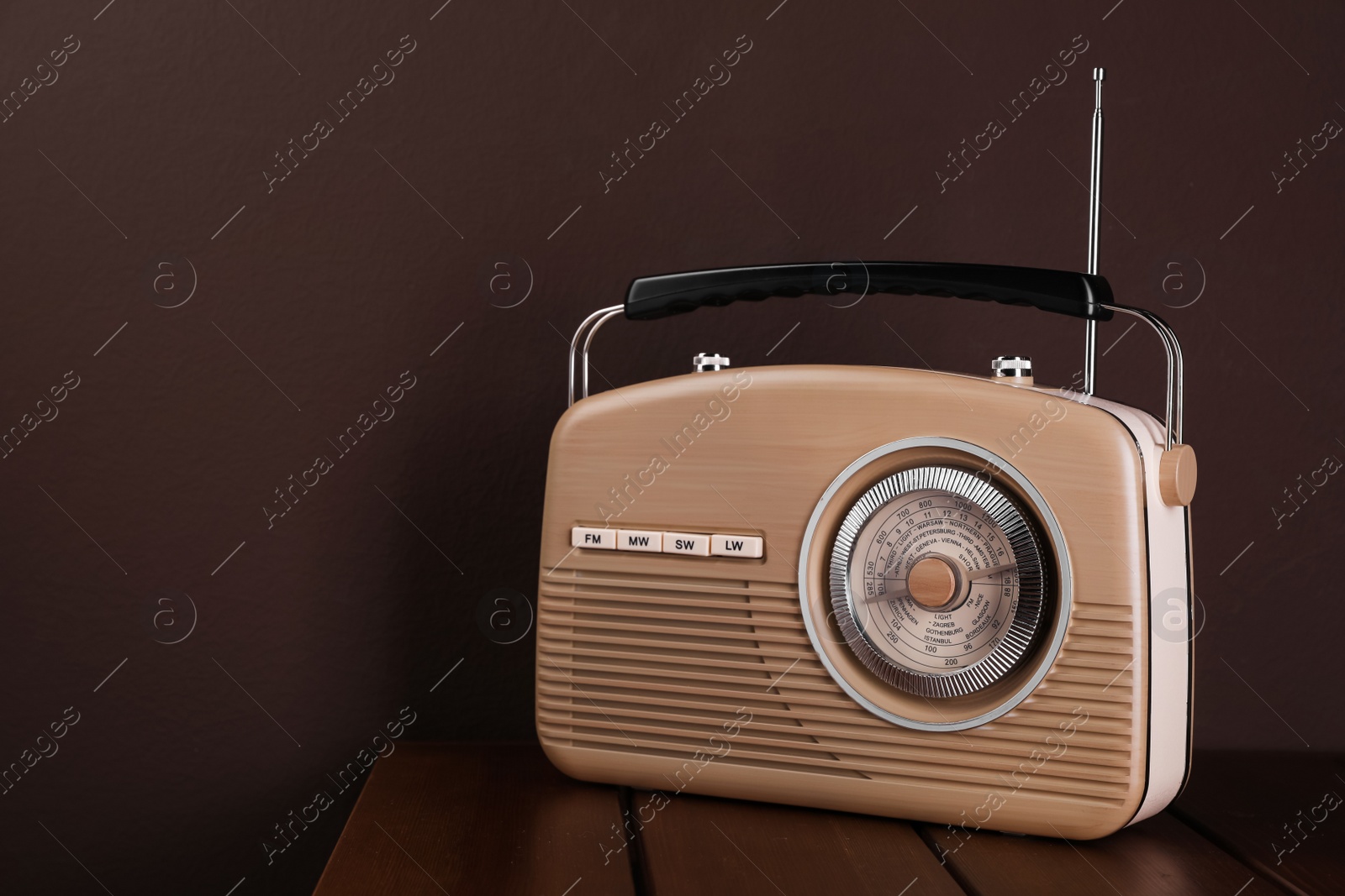 Photo of Retro radio receiver on wooden table against brown background. Space for text