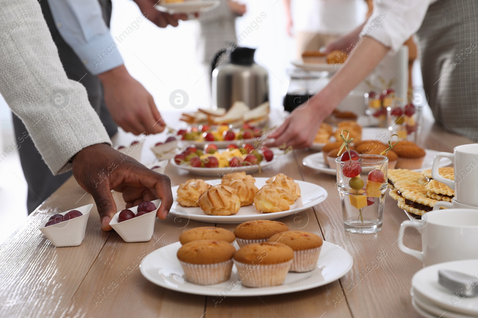 Photo of People near table with different delicious snacks during coffee break, closeup