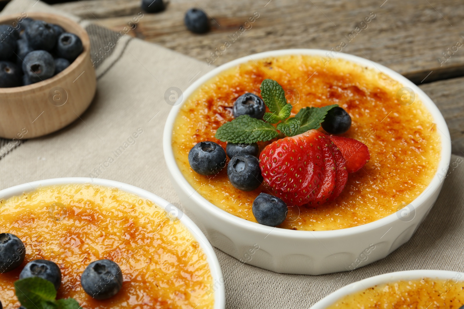 Photo of Delicious creme brulee with berries and mint in bowls on wooden table, closeup