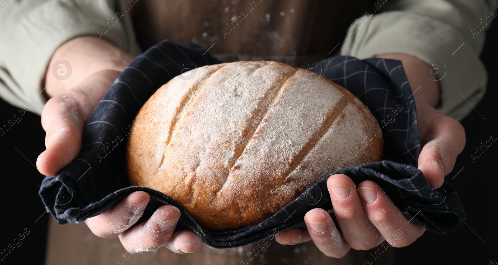 Photo of Woman holding freshly baked bread on black background, closeup