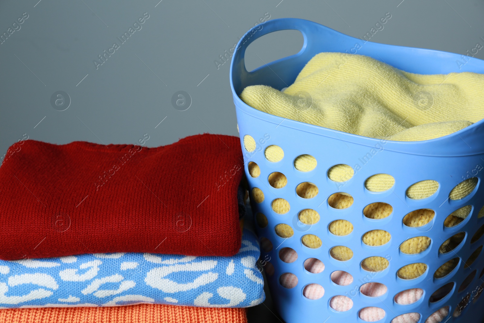 Photo of Plastic laundry basket and clean clothes on grey background, closeup