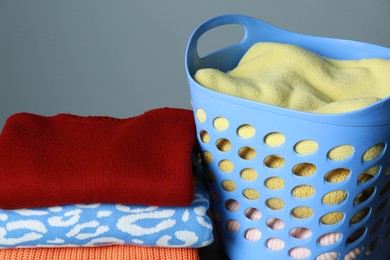 Photo of Plastic laundry basket and clean clothes on grey background, closeup