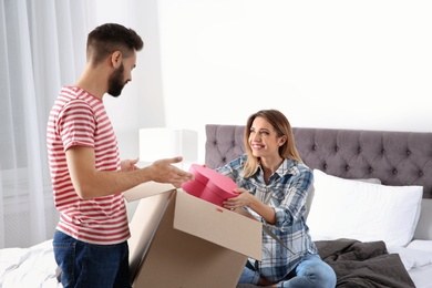 Photo of Young couple opening parcel in bedroom at home