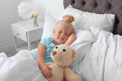 Cute little girl with teddy bear sleeping in bed