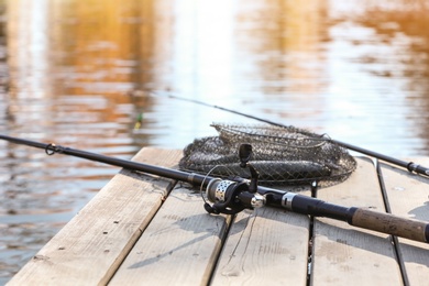 Photo of Fishing rods and fresh fish on wooden pier near pond