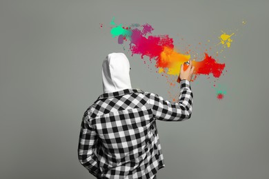 Image of Man spraying color paints on grey background, back view