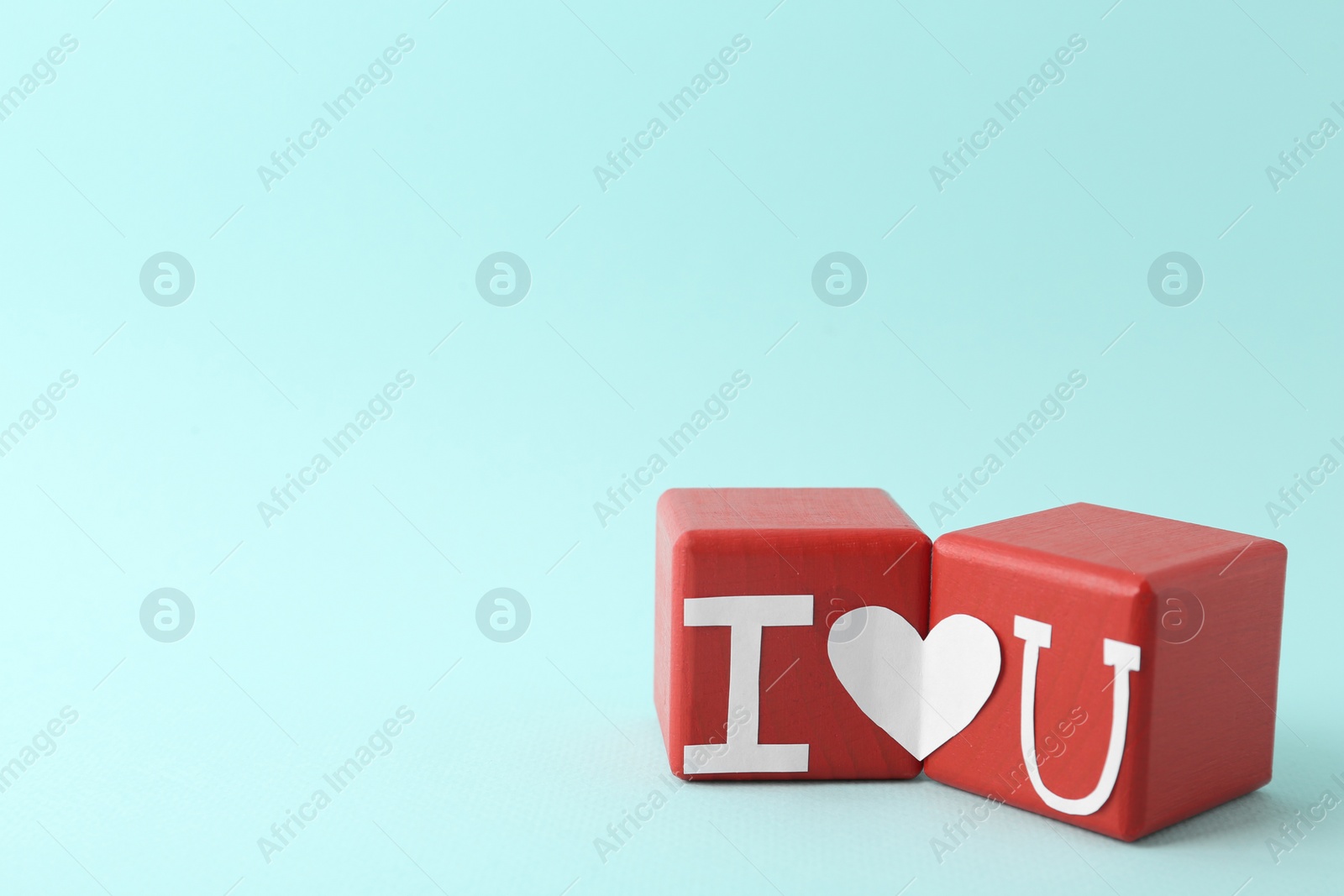 Photo of Phrase I Love You made of paper letters and heart connecting two red cubes on light blue background