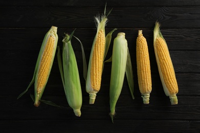 Photo of Tasty sweet corn cobs on wooden table, top view