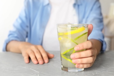 Woman with glass of citrus refreshing drink at grey marble table, closeup