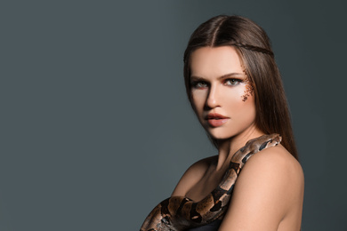 Photo of Beautiful woman with boa constrictor on grey background. Space for text