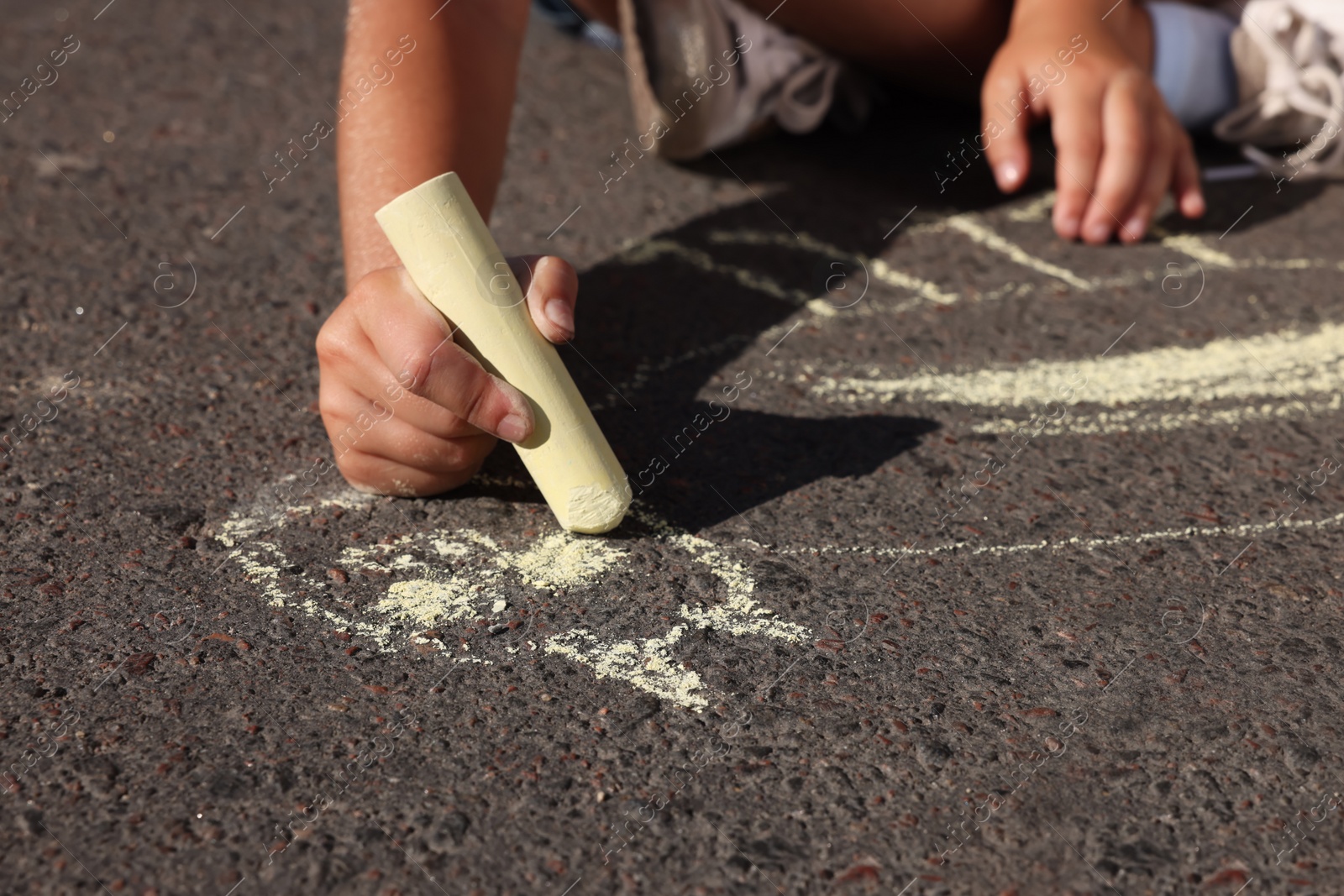 Photo of Little child drawing cat with colorful chalk on asphalt, closeup