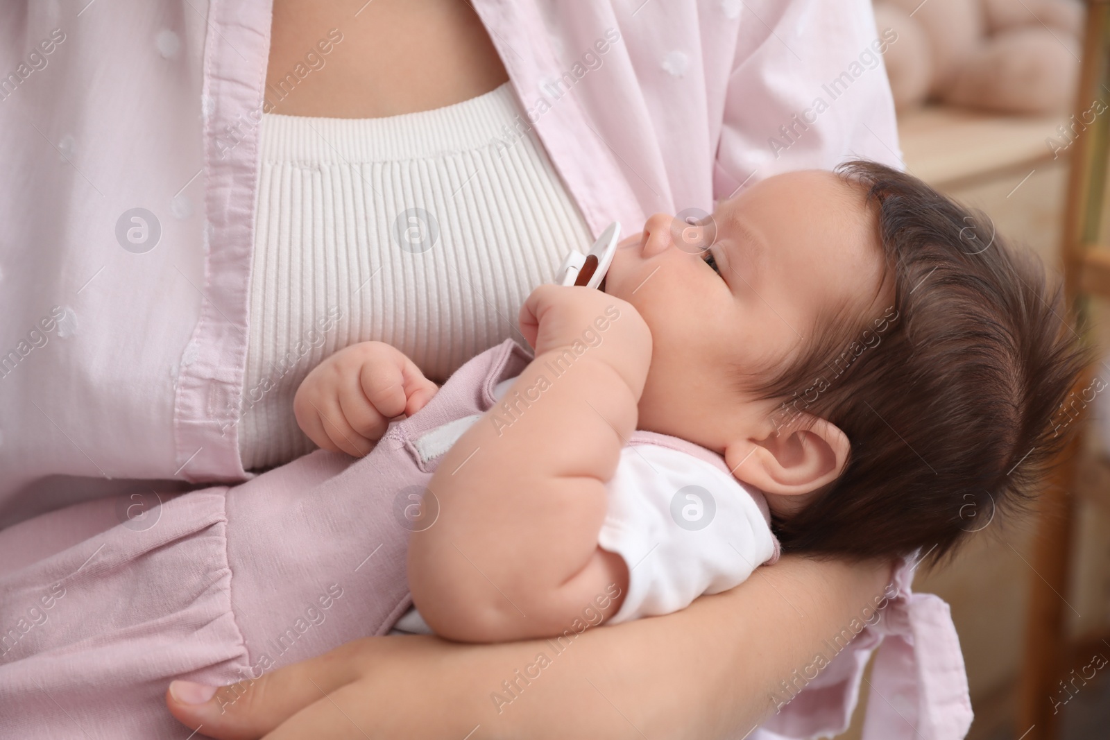 Photo of Mother holding her cute little baby with pacifier at home, closeup