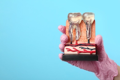 Photo of Dentist holding educational model of jaw section with teeth on color background. Space for text