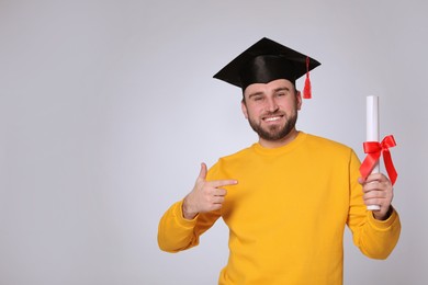 Photo of Happy student with graduation hat and diploma on grey background. Space for text