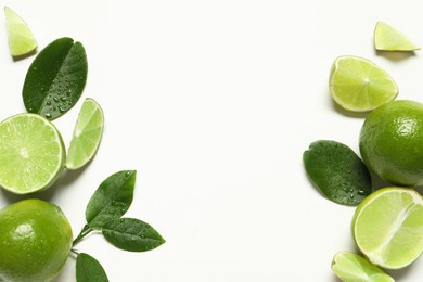 Whole and cut fresh ripe limes with green leaves on white background, flat lay