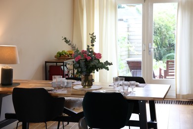 Stylish dining room with comfortable furniture, big window and bouquet of roses