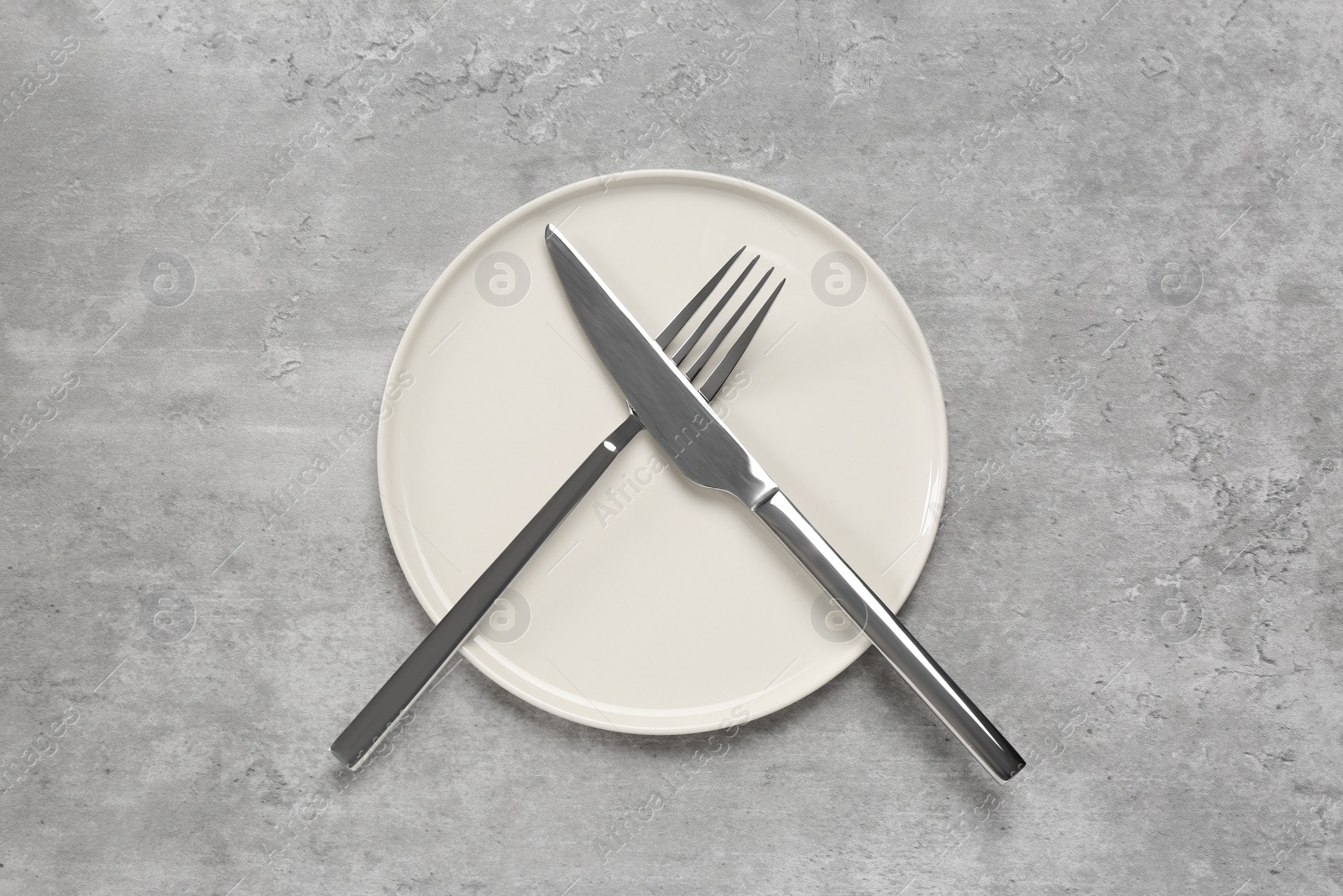 Photo of Clean plate with shiny silver cutlery on light grey table, flat lay