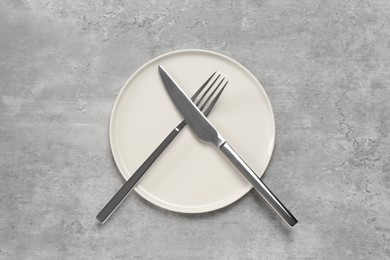 Clean plate with shiny silver cutlery on light grey table, flat lay