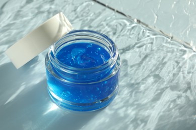 Photo of Open jar of cosmetic product on light blue background, space for text