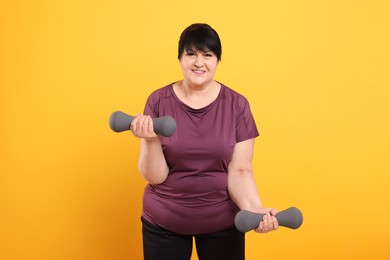 Photo of Happy overweight mature woman doing exercise with dumbbells on orange background