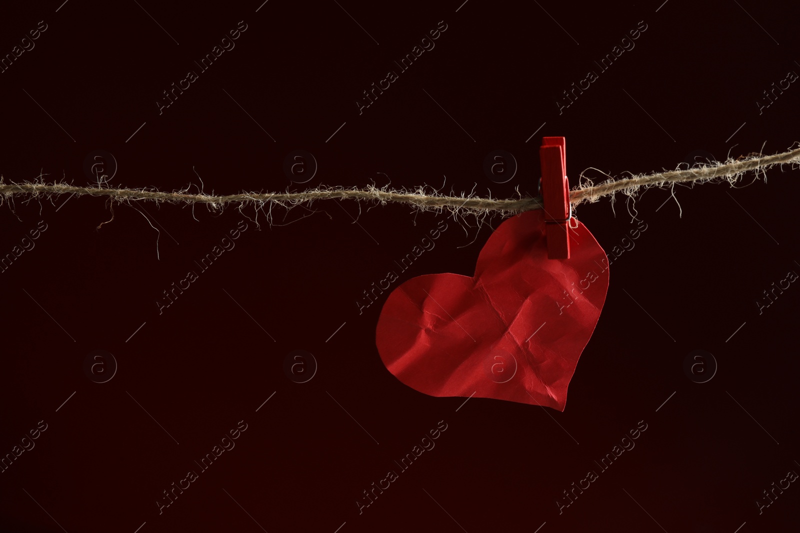 Photo of Crumpled red paper heart on rope against burgundy background, space for text. Broken heart