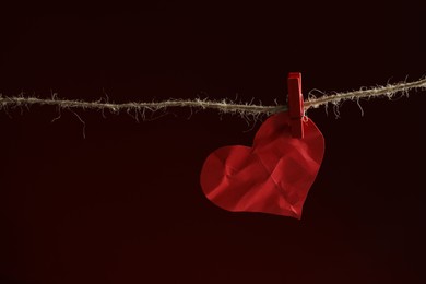 Crumpled red paper heart on rope against burgundy background, space for text. Broken heart