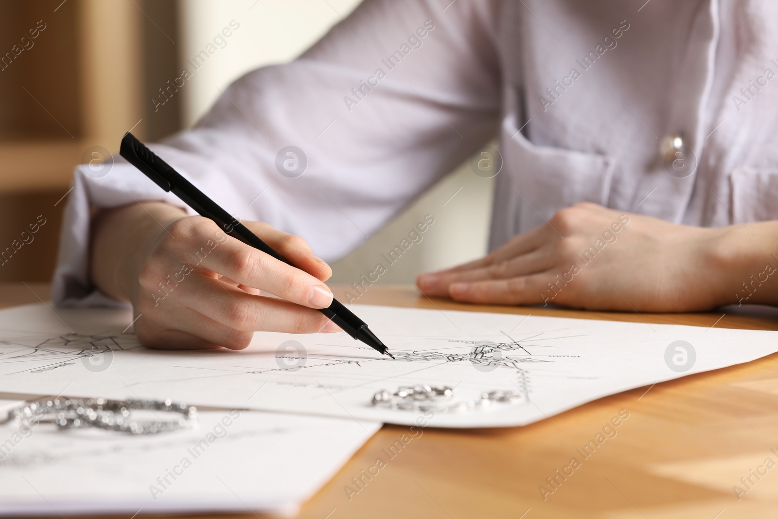 Photo of Jeweler drawing sketch of elegant necklace on paper at wooden table indoors, closeup