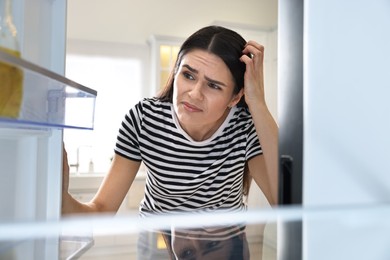 Photo of Upset woman near empty refrigerator in kitchen, view from inside