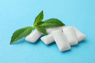 Photo of Tasty white chewing gums and mint leaves on light blue background, closeup