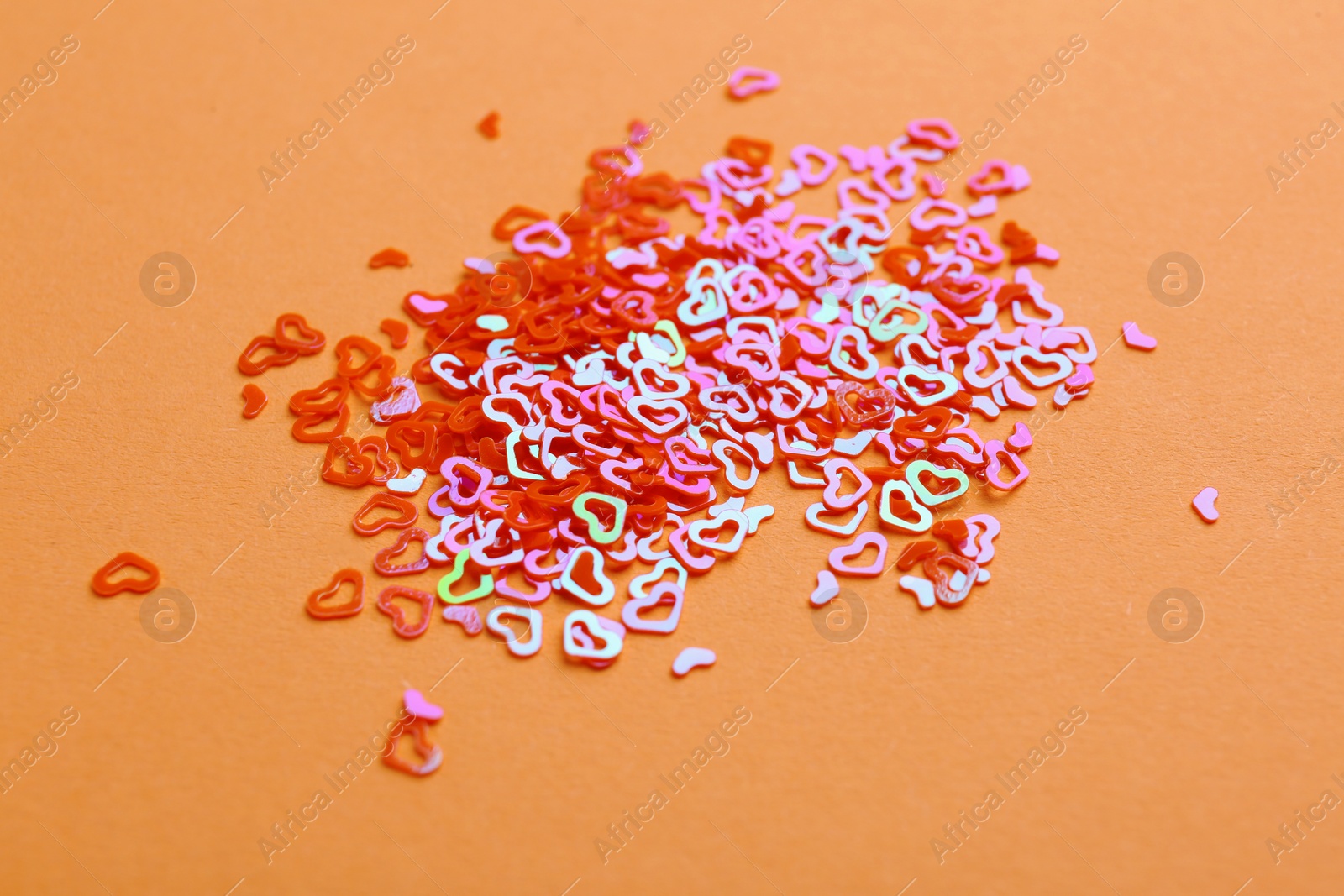 Photo of Shiny bright heart shaped glitter on beige background