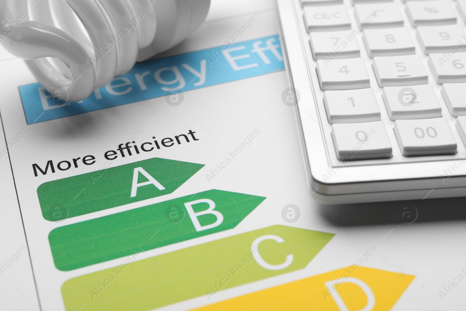 Photo of Energy efficiency rating chart, fluorescent light bulb and calculator, closeup