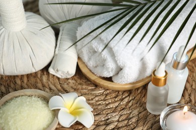 Photo of Composition with different spa products and plumeria flower on wicker mat, closeup