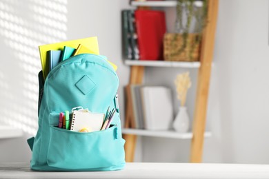 Turquoise backpack with school stationery on table indoors, space for text