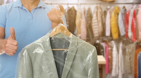 Dry-cleaning service. Man holding hanger with jacket in plastic bag indoors, space for text. Banner design