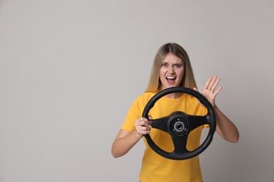 Photo of Emotional young woman with steering wheel on grey background. Space for text
