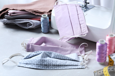 Photo of Sewing machine, homemade protective masks and craft accessories on grey table