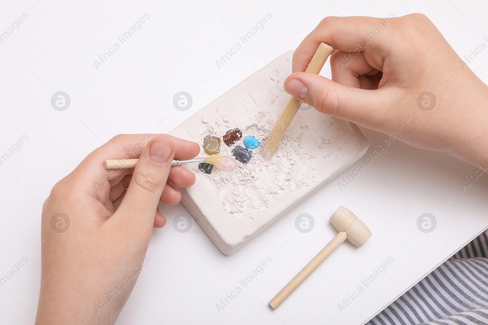 Photo of Child playing with Excavation kit at white table, above view. Educational toy for motor skills