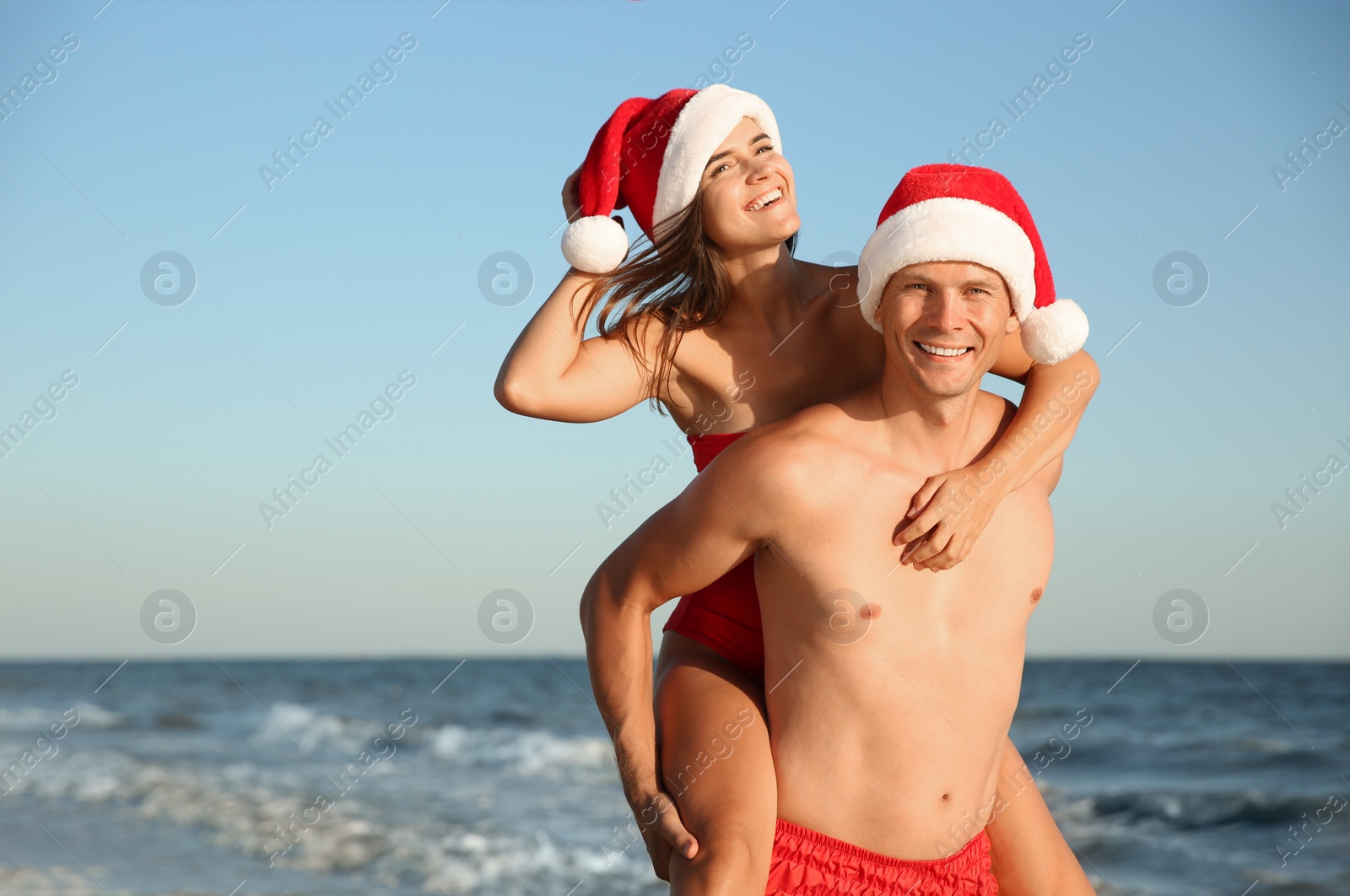 Photo of Happy couple with Santa hats together on beach. Christmas vacation