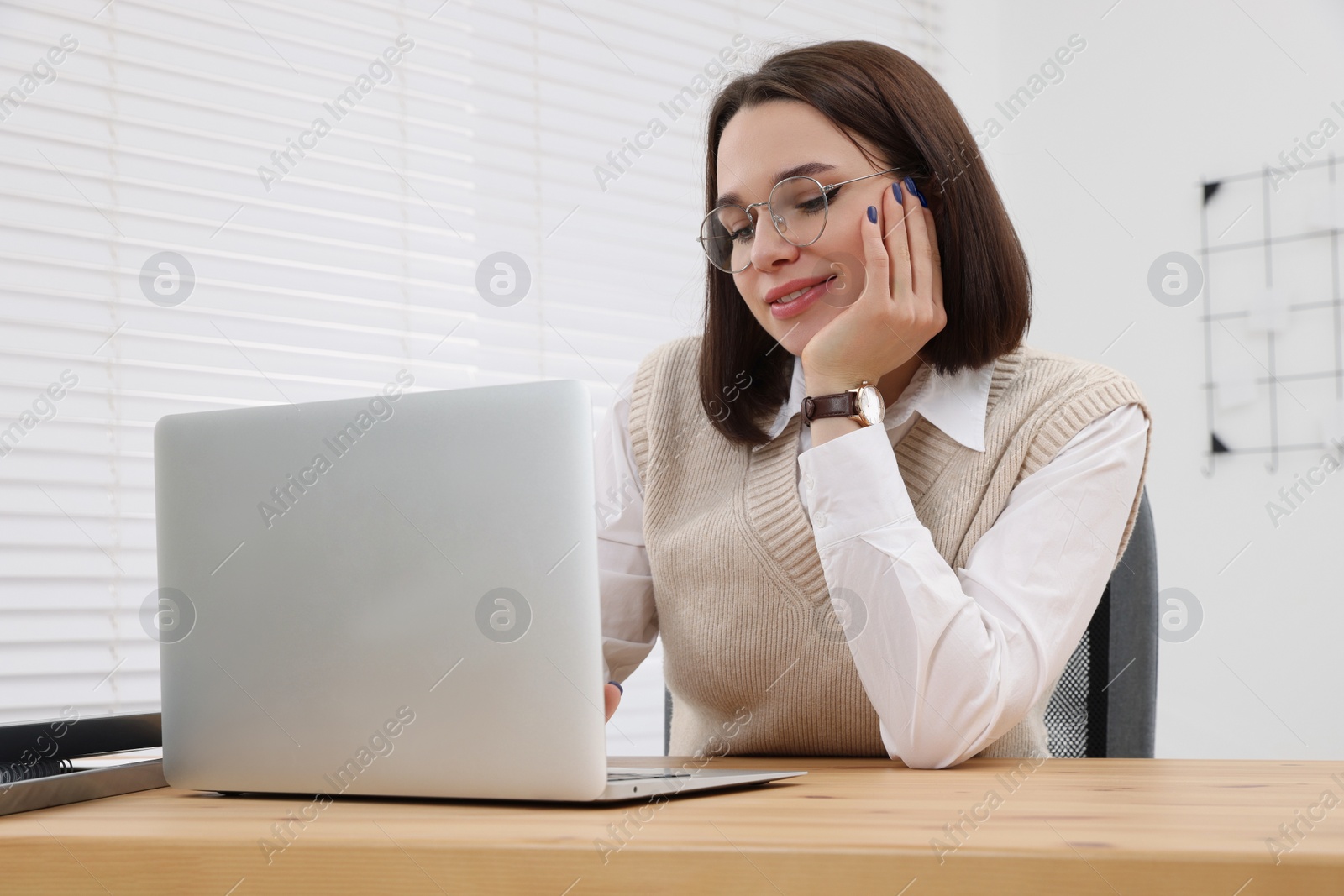 Photo of Happy young intern working with laptop at table in modern office