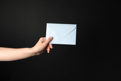 Woman holding white paper envelope on black background, closeup