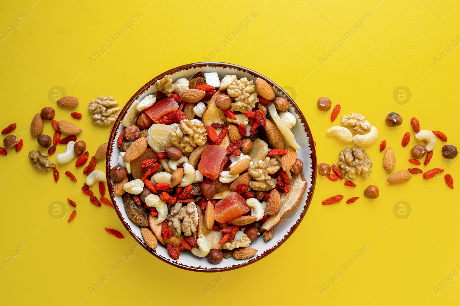 Photo of Bowl with mixed dried fruits and nuts on yellow background, flat lay