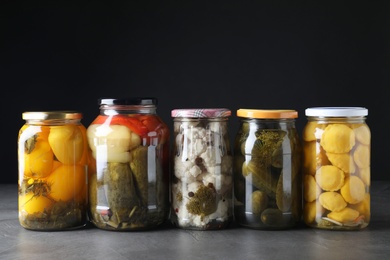 Photo of Jars of tasty pickled vegetables on grey table