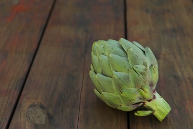 Photo of Whole fresh raw artichoke on wooden table, closeup. Space for text