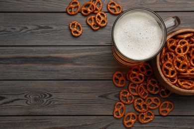 Delicious pretzel crackers and glass of beer on wooden table, flat lay. Space for text