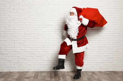 Authentic Santa Claus with bag full of gifts against white brick wall. Space for text