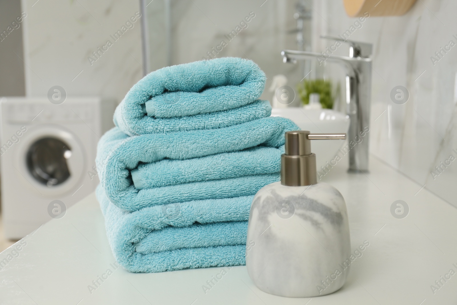 Photo of Stack of clean towels and soap dispenser on countertop in bathroom