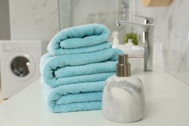 Stack of clean towels and soap dispenser on countertop in bathroom