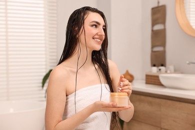 Young woman with jar of hair mask in bathroom