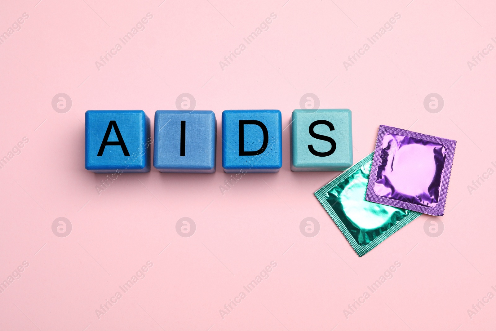 Photo of Word AIDS made with colorful cubes and condoms on pink background, flat lay. Safe sex